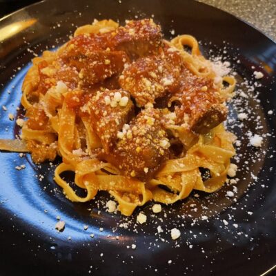 A plate of pasta with meat and sauce on it.