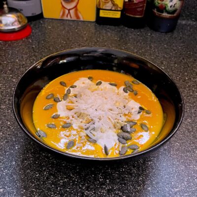 A bowl of soup with pumpkin seeds and parmesan cheese.