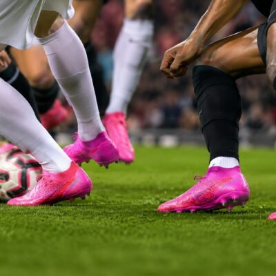 Soccer players wearing hot pink cleats on a green grass field during a match