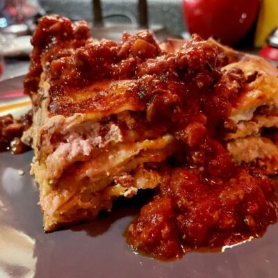 A piece of lasagna on a plate with sauce on it.