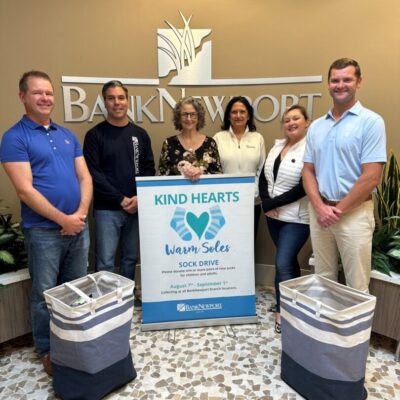 A group of people standing in front of a sign that says BankNewport and kind hearts.