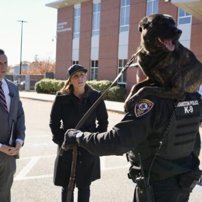 A police officer with a police dog talking to two civilians outside.