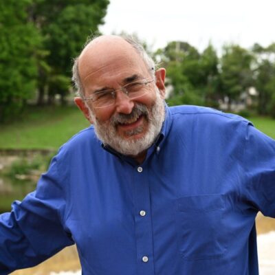 A man with glasses and a beard standing near a river.