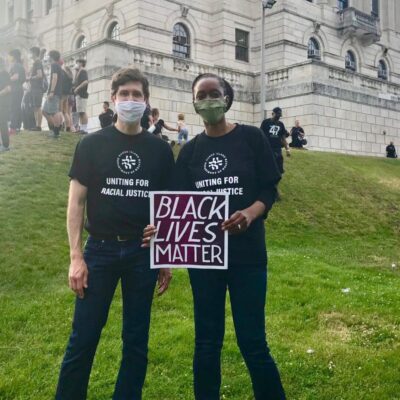 Two people holding a black lives matter sign in front of a building.