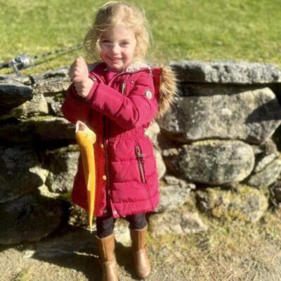 A little girl in a red coat standing next to a stone wall.