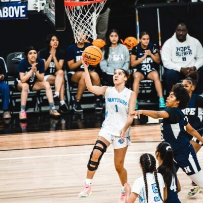 Woman shoots basketball in game.