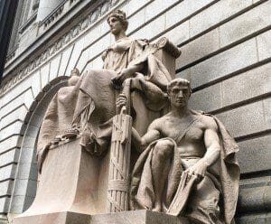 A statue of a woman sitting on a bench in front of a building.