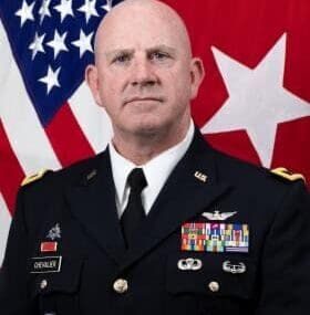 A man in military uniform with an american flag behind him.