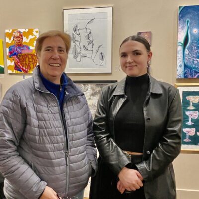 Two women standing in front of art displayed on a wall.