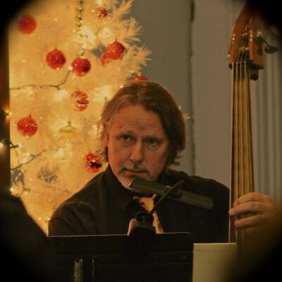 A man playing a bass in front of a christmas tree.