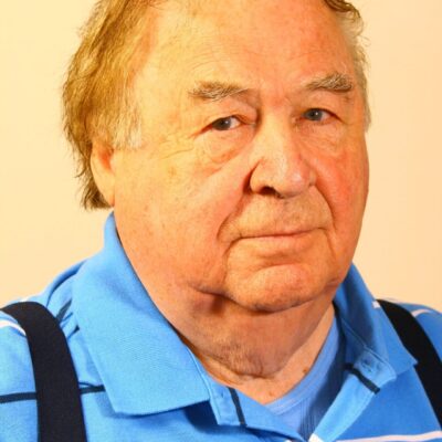 An older man wearing a blue shirt and suspenders.