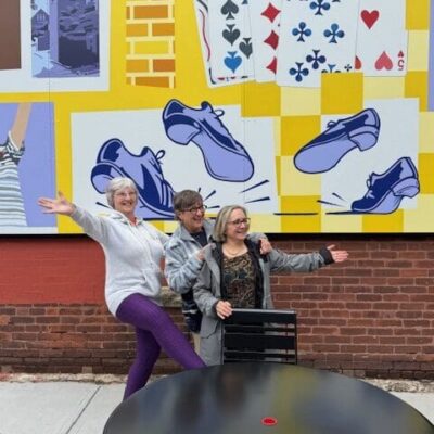 Two women are posing for a picture in front of a mural.