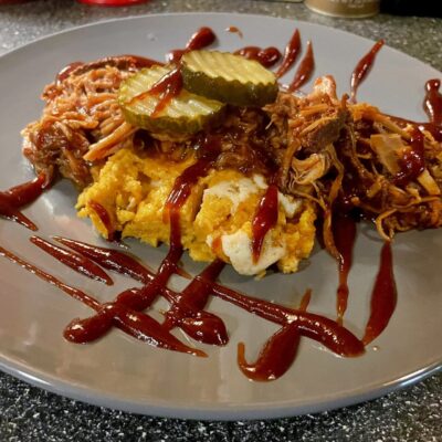 A plate with pulled pork and pickles on it.