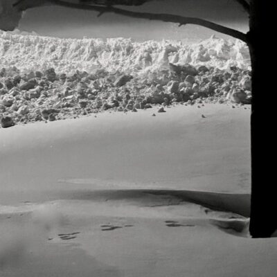 Snow-covered landscape viewed through a window with footprints in the snow.