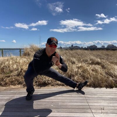 A man squatting on a boardwalk near the water.