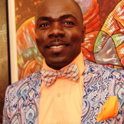 A black man in a blue suit and orange bow tie.