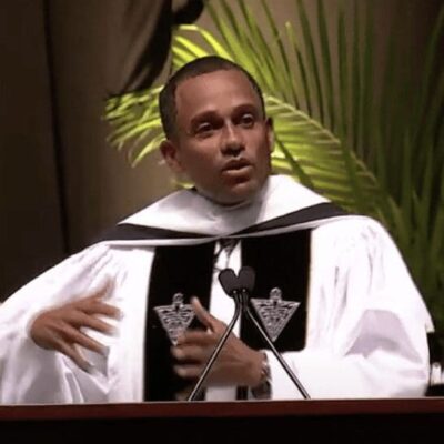 Hill Harper, a man in a robe, speaking into a microphone at Providence College.
