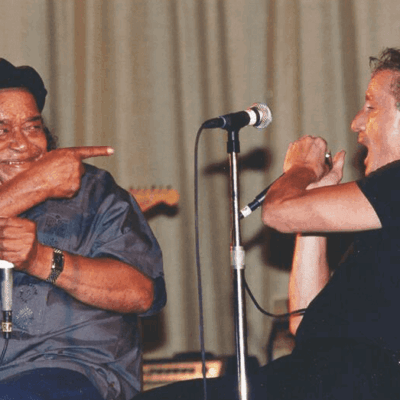 Two men sitting on stage with microphones in front of them.