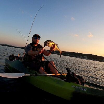 A man holding a fish in a kayak at sunset.
