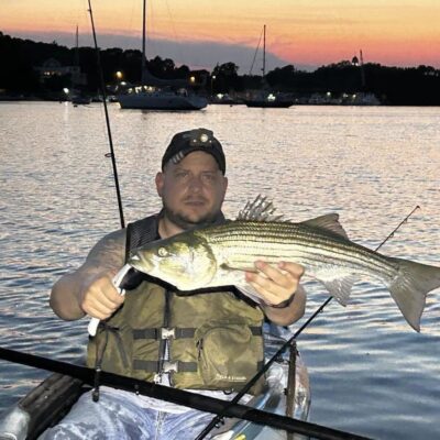 Man holding large striped bass in kayak.