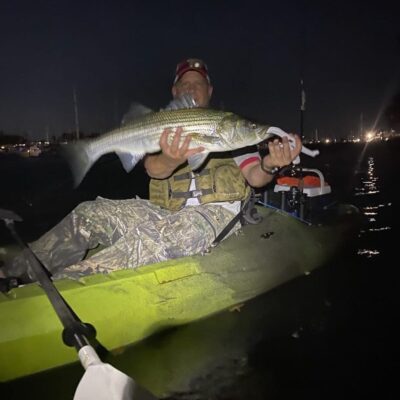A man in a kayak holding a striped bass.