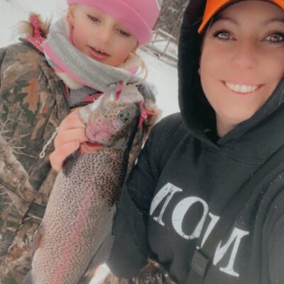 Two women holding up a rainbow trout in the snow.