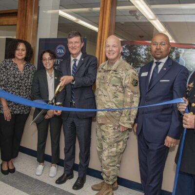 A group of people cutting a ribbon in front of a military building.