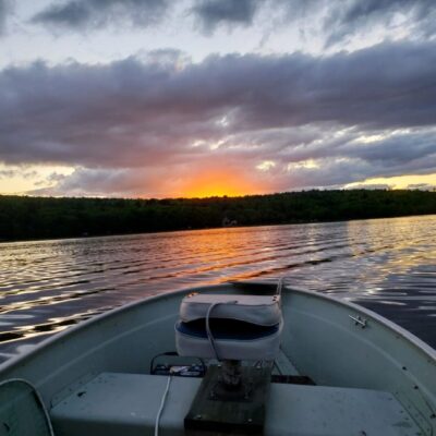 A boat on a lake with a sun setting behind it.