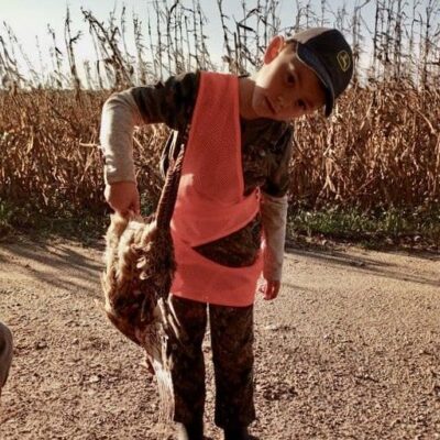 A young boy holding a dead bird in a corn field.