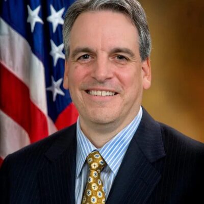 A man in a suit and tie standing in front of an american flag.