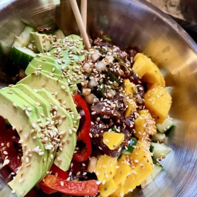 A bowl full of vegetables and fruit with chopsticks.