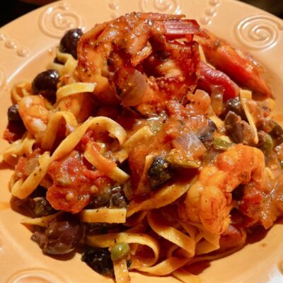 A plate of pasta with shrimp, olives and tomatoes.