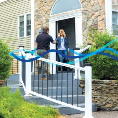A couple standing outside a house entrance with a white fence in front.