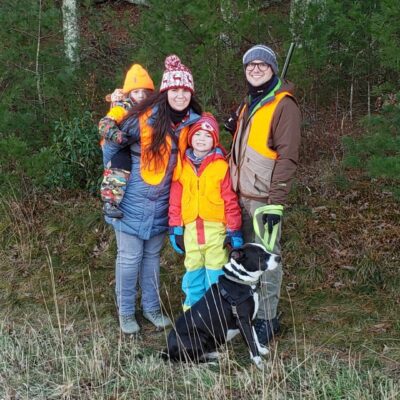 A family poses for a photo in a wooded area with a dog.