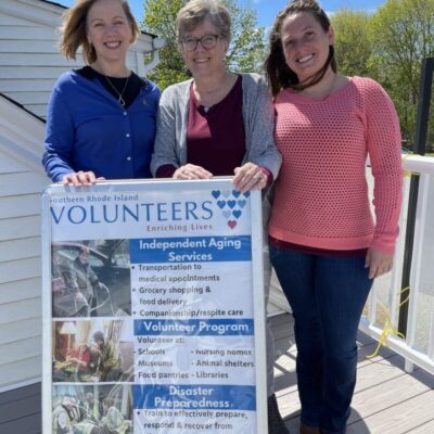Three women standing in front of a sign that says volunteers.