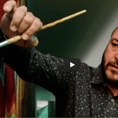 A man holding a paint brush in front of a colorful painting.