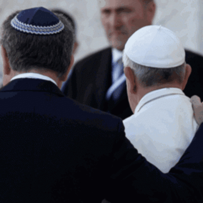 A man in a suit is hugging a man in a kippah.