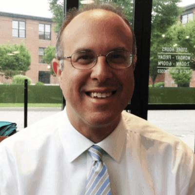 A man wearing glasses and a blue tie is smiling.