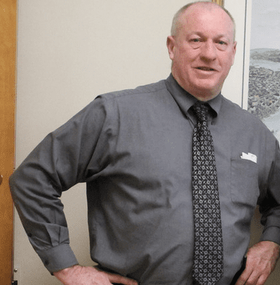 A man in a gray shirt standing next to a picture.