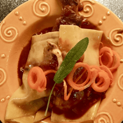 A plate of pasta with sauce and sprigs of sage.