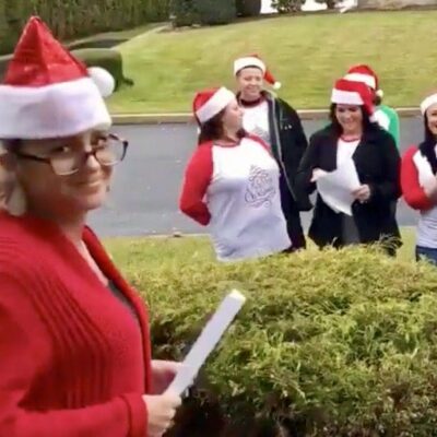 A group of people in santa hats standing in front of bushes.