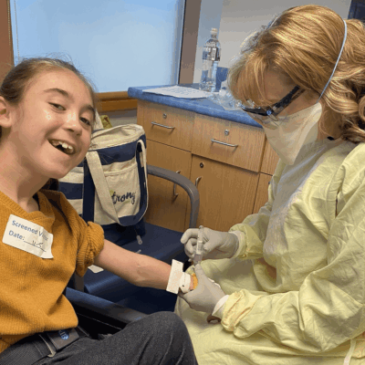 A young girl in a wheelchair getting her arm swabbed by a nurse.