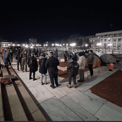 A group of people standing on a sidewalk at night.