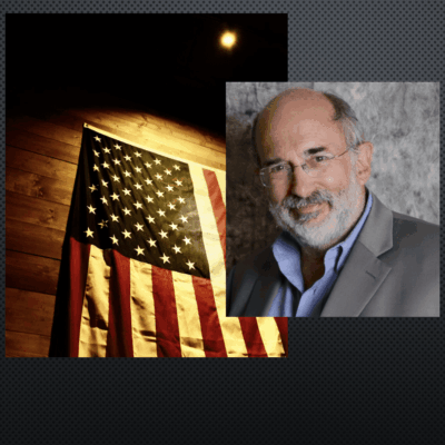 A man with a beard and glasses is standing next to an american flag.
