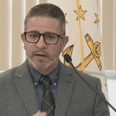 A man in a suit and tie speaking into a microphone.