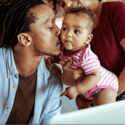 A man and woman kissing a baby in front of a laptop.