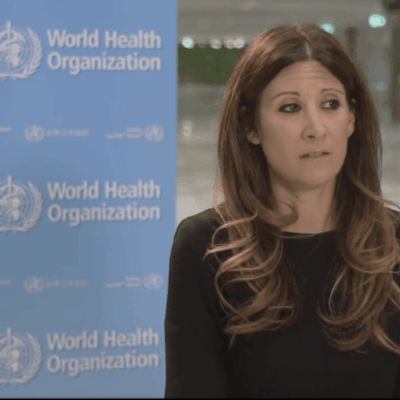 A woman in front of a world health organization sign.