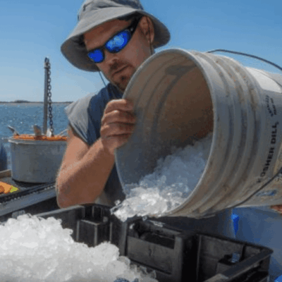 A man pouring ice into a bucket on a boat.