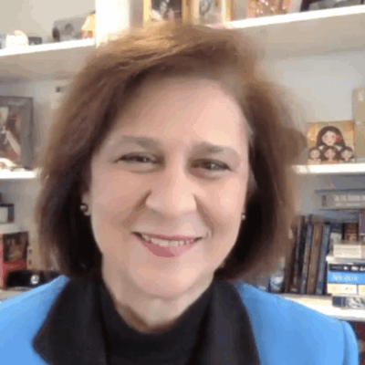 A woman in a blue jacket smiling in front of a bookshelf.
