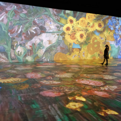 A woman is standing in front of a large projection of flowers.